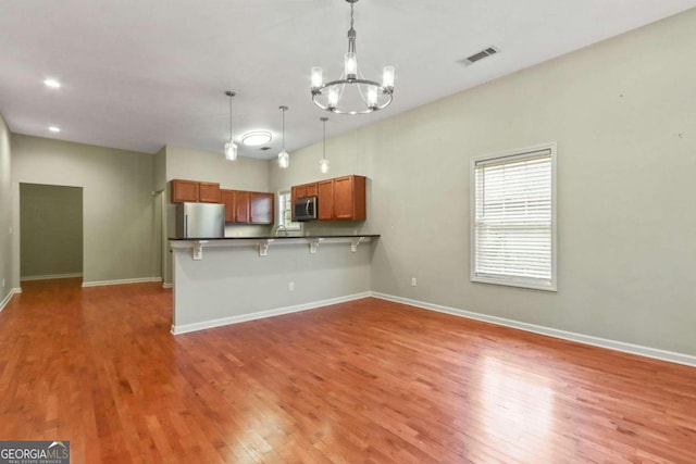 kitchen featuring wood-type flooring, appliances with stainless steel finishes, kitchen peninsula, pendant lighting, and a breakfast bar