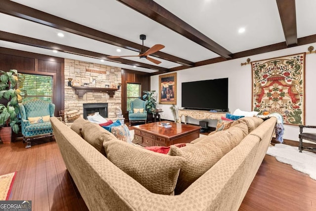 living area featuring a ceiling fan, a fireplace, beamed ceiling, and wood finished floors