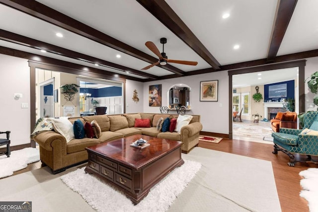 living area with arched walkways, a fireplace, baseboards, light wood-style floors, and beamed ceiling