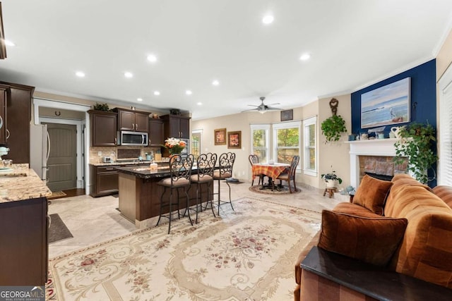 kitchen featuring ornamental molding, stainless steel appliances, dark brown cabinets, and open floor plan