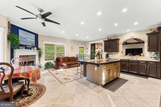 kitchen featuring a stone fireplace, dark brown cabinetry, decorative backsplash, a breakfast bar area, and a center island