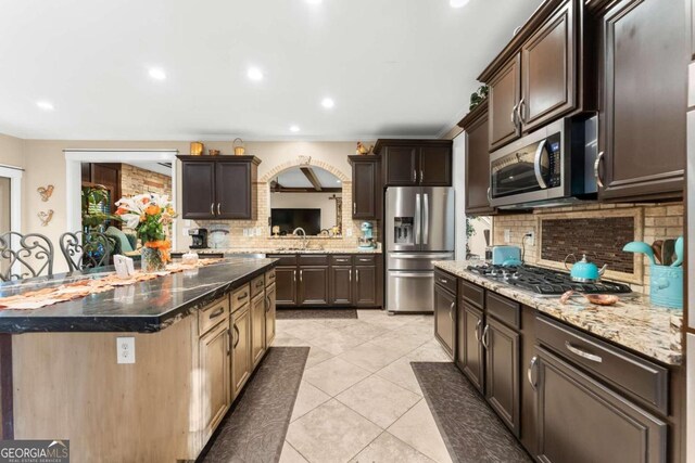 kitchen featuring stainless steel dishwasher, dark brown cabinets, dark stone countertops, and plenty of natural light