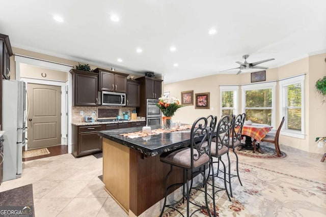 kitchen with appliances with stainless steel finishes, ornamental molding, a kitchen bar, backsplash, and a center island