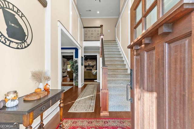 entrance foyer featuring a high ceiling, dark wood-style flooring, visible vents, ornamental molding, and stairway