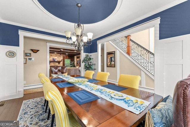 dining room featuring a baseboard radiator, ornamental molding, wood finished floors, an inviting chandelier, and stairs