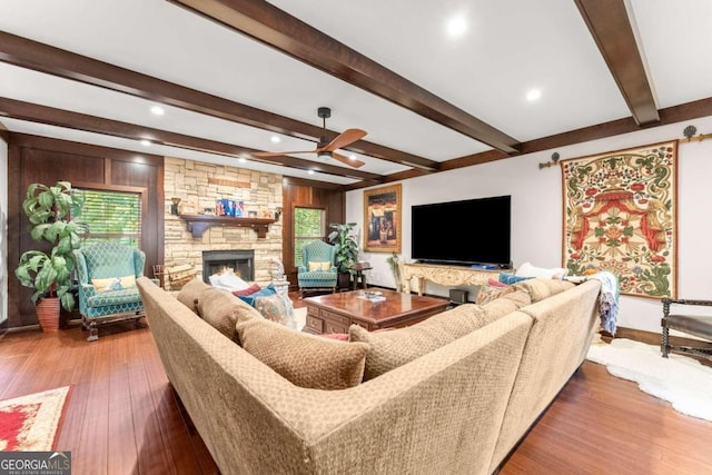 living area featuring beamed ceiling, a fireplace, wood finished floors, and a ceiling fan