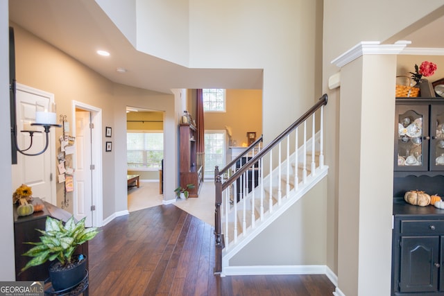 foyer entrance featuring decorative columns, a towering ceiling, ornamental molding, and dark hardwood / wood-style floors