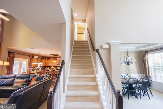 staircase featuring carpet, a notable chandelier, and a towering ceiling