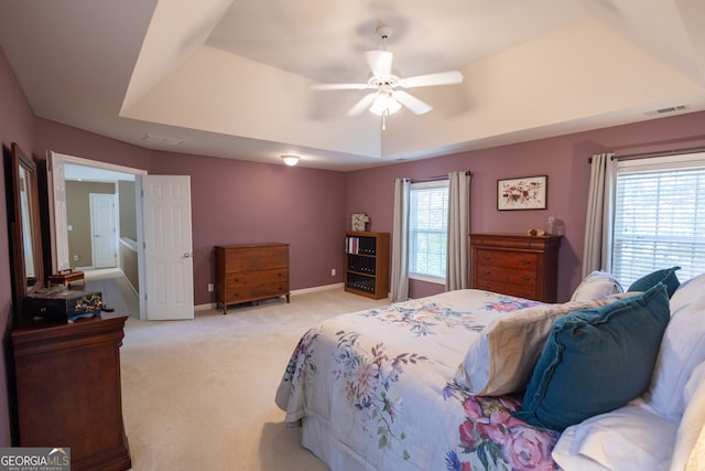 carpeted bedroom featuring ceiling fan, a raised ceiling, and multiple windows