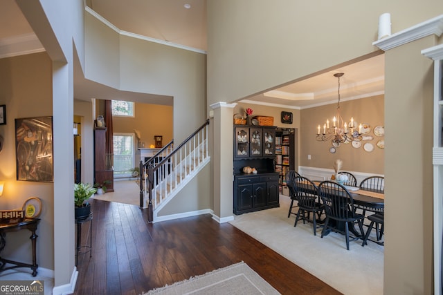 dining space with a notable chandelier, dark wood-type flooring, ornate columns, a towering ceiling, and crown molding