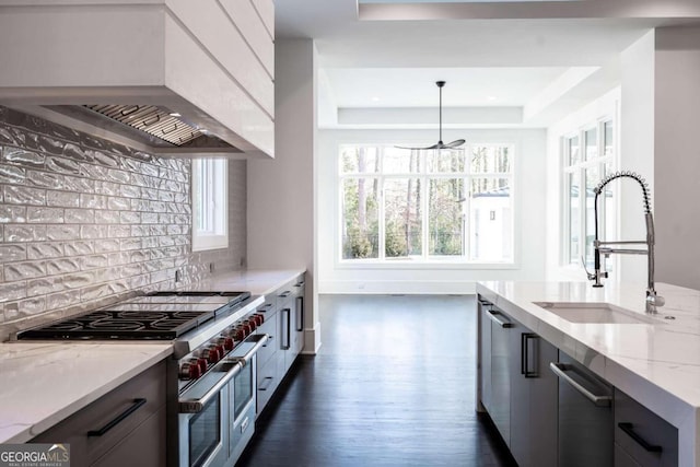 kitchen with wall chimney range hood, dark wood-type flooring, hanging light fixtures, stainless steel appliances, and light stone countertops