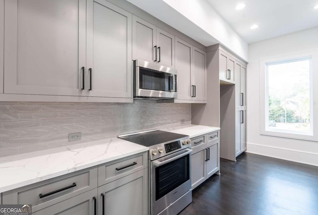 kitchen with dark wood-type flooring, stainless steel appliances, light stone countertops, gray cabinets, and tasteful backsplash