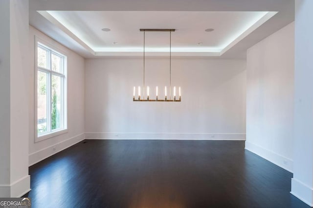 empty room featuring a notable chandelier, dark hardwood / wood-style floors, and a tray ceiling