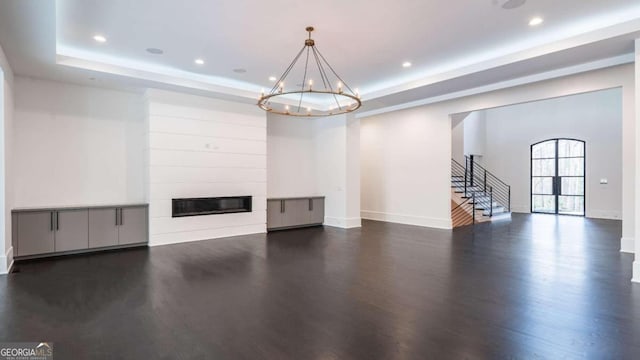 unfurnished living room with dark wood-type flooring, an inviting chandelier, a tray ceiling, and a fireplace