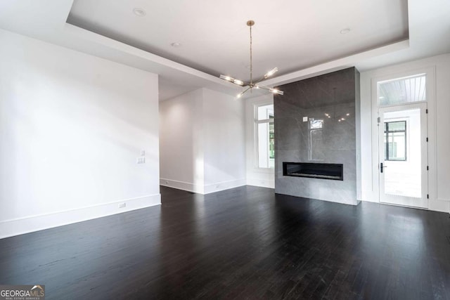 unfurnished living room featuring a notable chandelier, a fireplace, dark hardwood / wood-style floors, and a raised ceiling