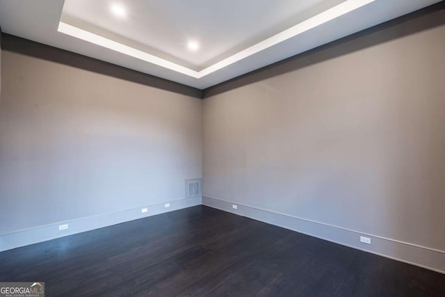 empty room with dark hardwood / wood-style floors and a tray ceiling