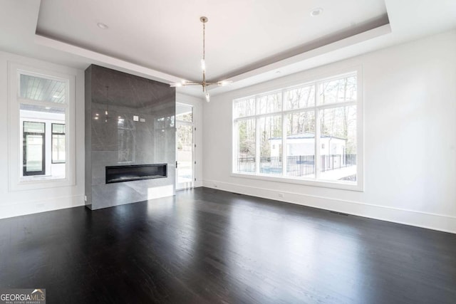 unfurnished living room with a large fireplace, a raised ceiling, dark hardwood / wood-style flooring, and an inviting chandelier