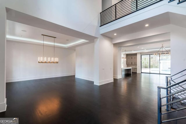 unfurnished living room featuring a raised ceiling, an inviting chandelier, and dark hardwood / wood-style flooring