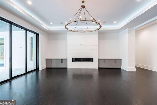 unfurnished living room featuring dark hardwood / wood-style floors, a chandelier, a large fireplace, and a tray ceiling