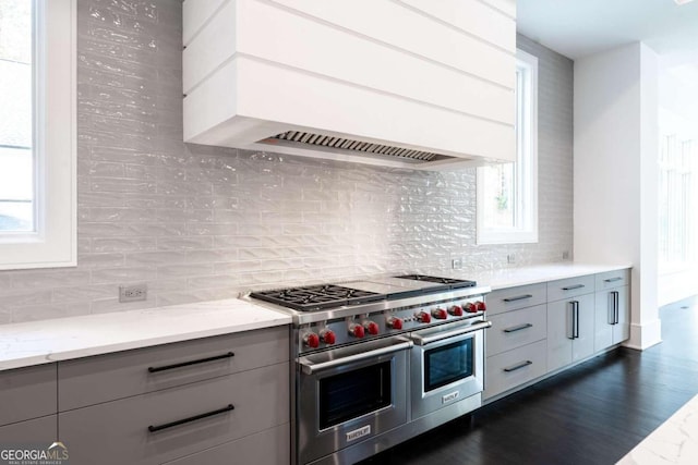 kitchen with custom range hood, range with two ovens, light stone countertops, and a healthy amount of sunlight