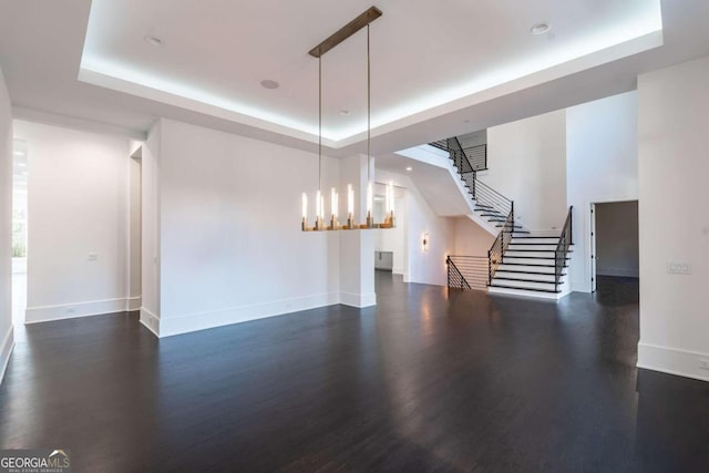 unfurnished living room with a notable chandelier, a raised ceiling, and dark hardwood / wood-style floors