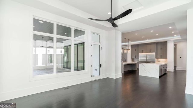 unfurnished living room featuring ceiling fan, sink, dark wood-type flooring, and a raised ceiling