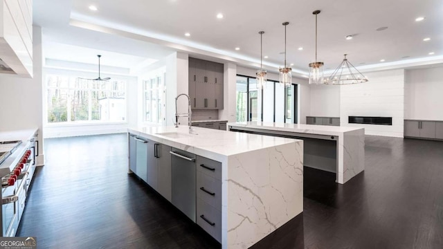 kitchen with hanging light fixtures, dark hardwood / wood-style flooring, a spacious island, light stone countertops, and sink