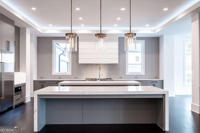 kitchen featuring a spacious island, light stone counters, sink, and pendant lighting