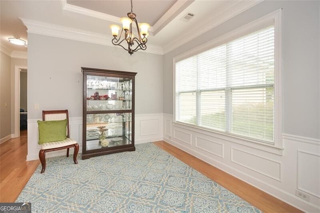 sitting room featuring light hardwood / wood-style flooring, an inviting chandelier, ornamental molding, and a raised ceiling