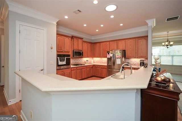 kitchen featuring kitchen peninsula, tasteful backsplash, light hardwood / wood-style flooring, a notable chandelier, and stainless steel appliances