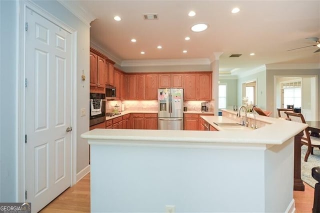 kitchen with sink, ceiling fan, stainless steel appliances, ornamental molding, and light hardwood / wood-style flooring