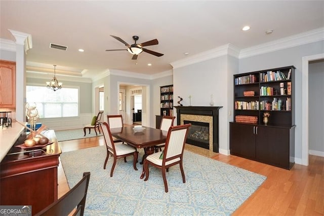 dining room featuring light hardwood / wood-style floors, crown molding, and ceiling fan with notable chandelier