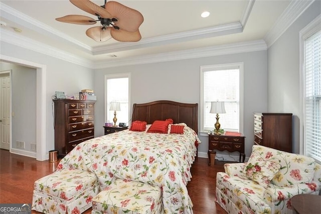 bedroom with crown molding, dark hardwood / wood-style floors, a tray ceiling, and ceiling fan