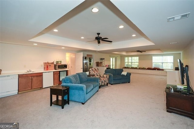 living room with ceiling fan, light carpet, and a tray ceiling