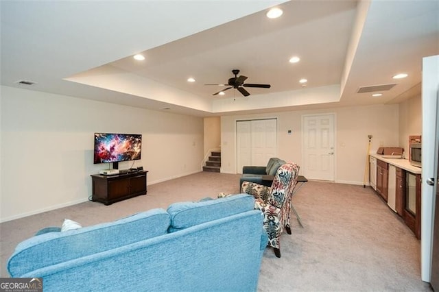 living room with light carpet, ceiling fan, and a raised ceiling