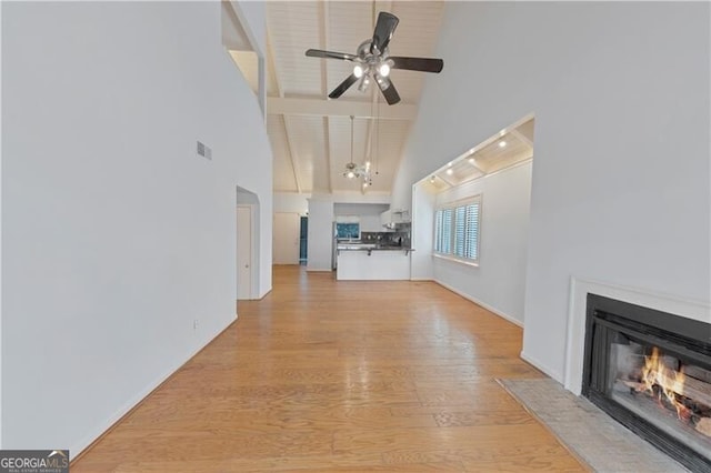 unfurnished living room with light hardwood / wood-style flooring, high vaulted ceiling, and ceiling fan with notable chandelier