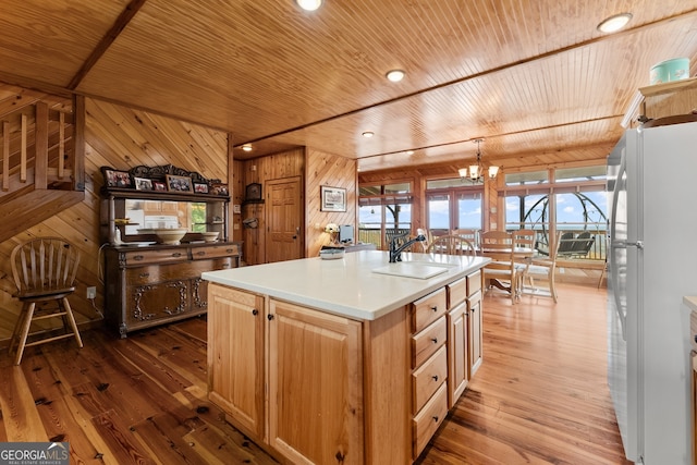 kitchen featuring hardwood / wood-style flooring, sink, an island with sink, wooden walls, and white fridge