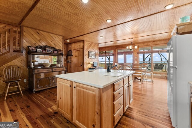 kitchen with sink, wood ceiling, a kitchen island with sink, wooden walls, and white fridge