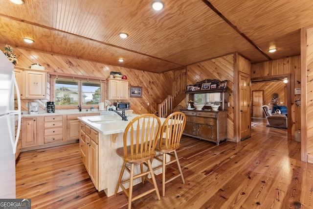 kitchen featuring light brown cabinets, hardwood / wood-style flooring, wooden walls, and sink