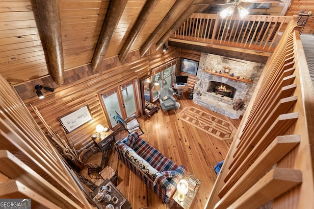 living room with beamed ceiling, high vaulted ceiling, wood-type flooring, a stone fireplace, and wooden walls