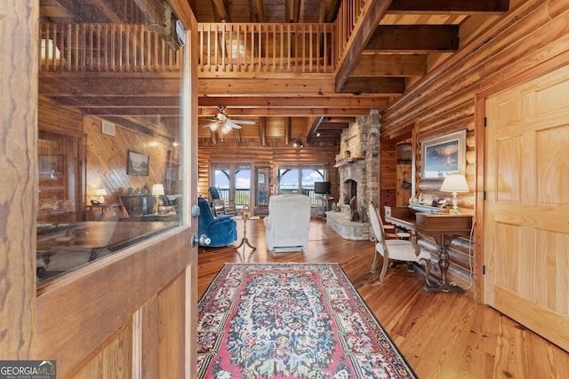 interior space with a high ceiling, a stone fireplace, log walls, and hardwood / wood-style flooring