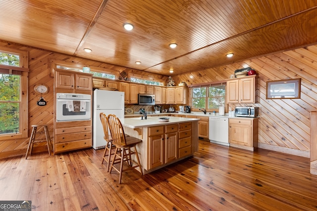 kitchen with wood walls, white appliances, a center island with sink, and plenty of natural light