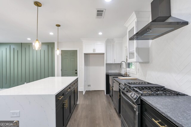 kitchen with gas range, dark wood-type flooring, wall chimney range hood, pendant lighting, and white cabinets