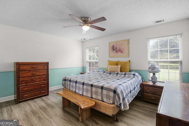 bedroom featuring light hardwood / wood-style flooring, a textured ceiling, multiple windows, and ceiling fan