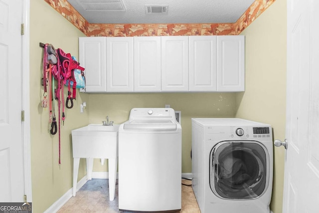 laundry area with independent washer and dryer, a textured ceiling, and cabinets