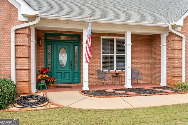 entrance to property with a porch, roof with shingles, and brick siding