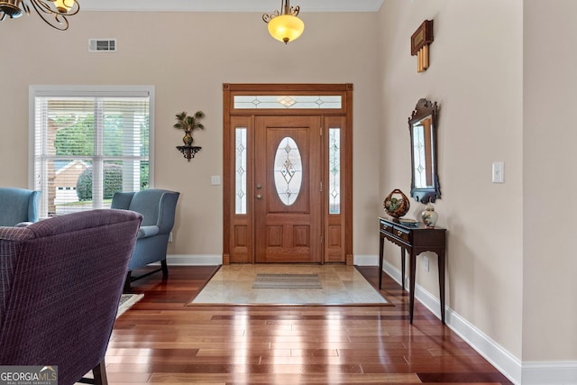 entrance foyer with a notable chandelier, baseboards, visible vents, and wood finished floors