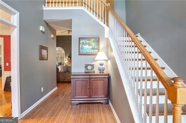 stairway with ceiling fan, wood-type flooring, and a high ceiling