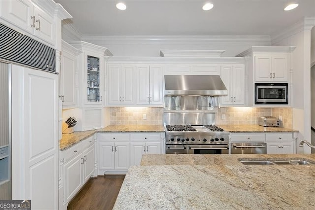 kitchen with dark hardwood / wood-style flooring, built in appliances, white cabinets, wall chimney exhaust hood, and ornamental molding