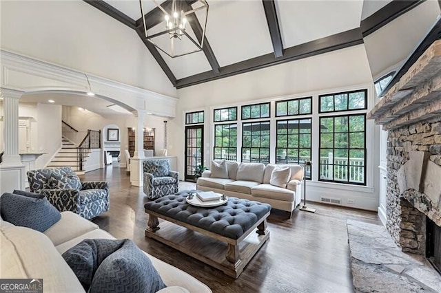 living room featuring beam ceiling, high vaulted ceiling, hardwood / wood-style floors, a stone fireplace, and decorative columns